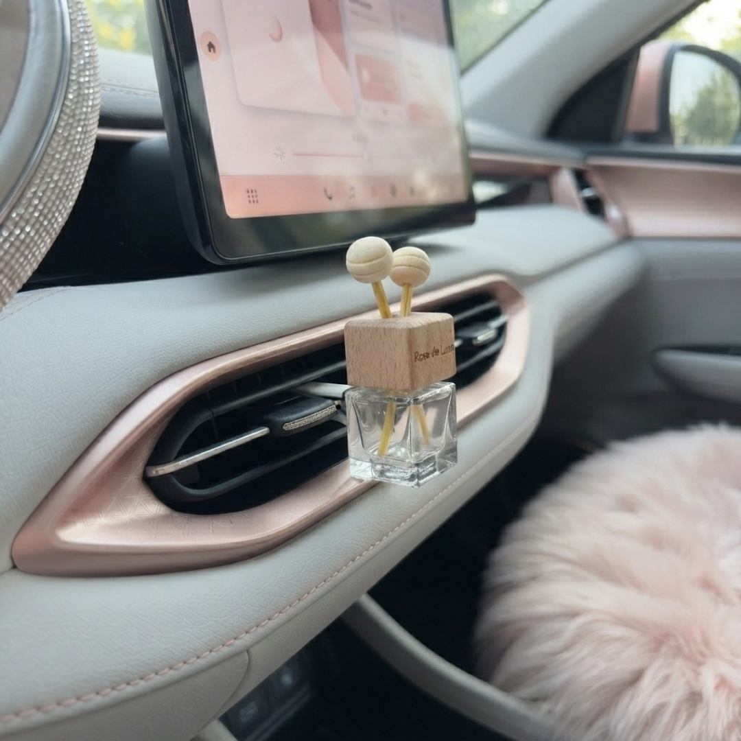 Prémium Rose de Luxe pálcás autós illatosító fából készült kupakkal és pálcákkal, elegáns, világos színű és rózsaarany keretes autóbelső szellőzőrácsára csíptetve.